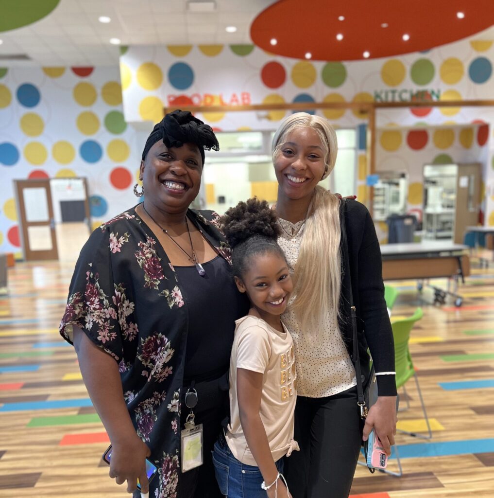 A case manager smiles next to a Positive Tomorrows student and her mother